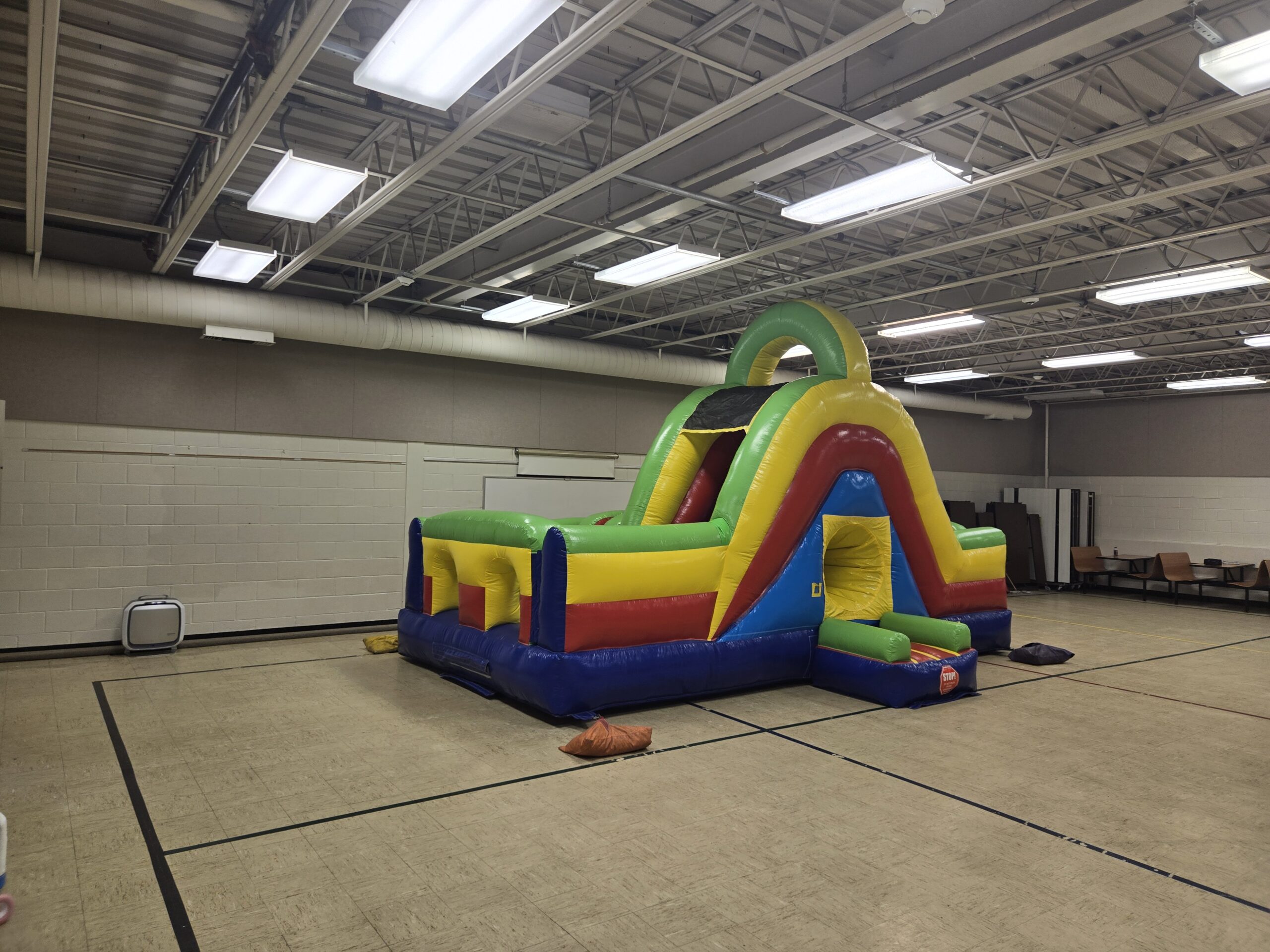 Colorful inflatable bounce-and-slide combination unit set up inside a gym