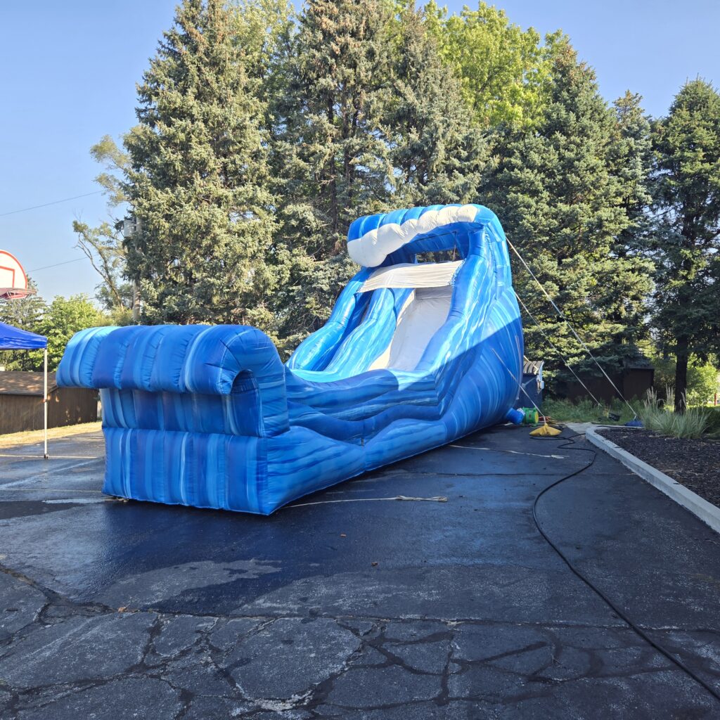 Papillion Water Slide Rentals selection featuring a blue wave-themed inflatable slide set up on pavement near trees