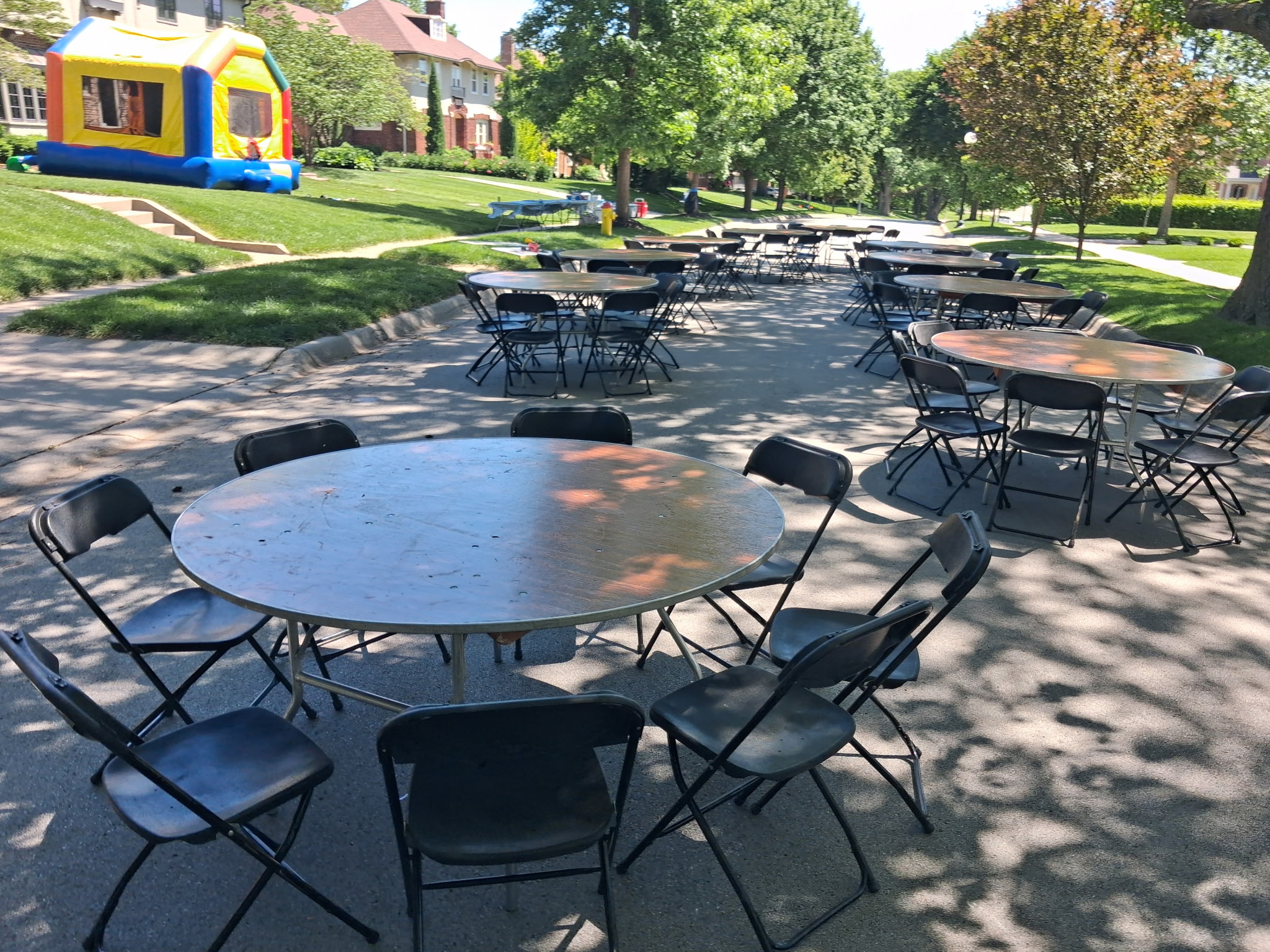 Backyard birthday party with inflatable, round tables, and black chairs